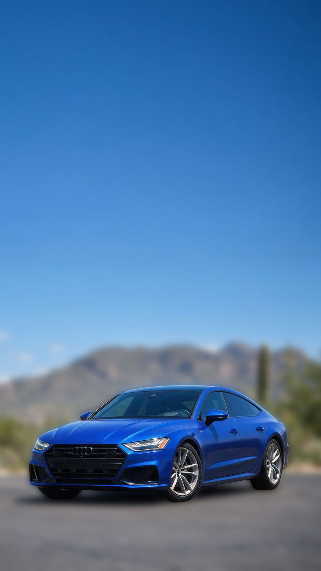 Blue Audi sedan detailed and gleaming on a Tucson desert road with mountain backdrop
